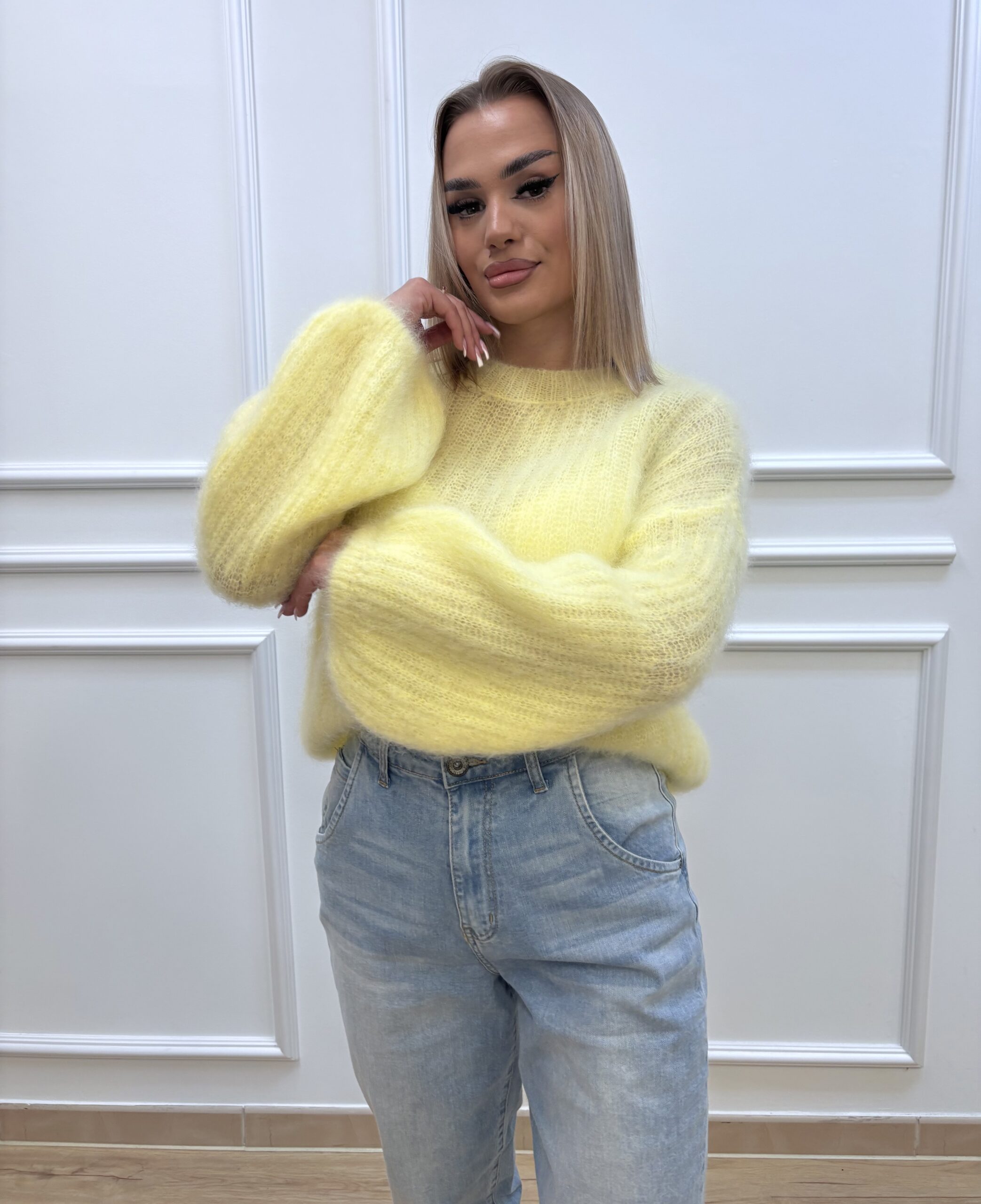 Modelka w żółtym swetrze moherowym z szerokimi rękawami i jasnoniebieskimi dżinsami, krzyżując ręce – kolekcja Secret Line